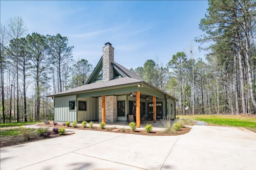 A modern house with a stone chimney, surrounded by trees and a landscaped yard, featuring a concrete driveway.