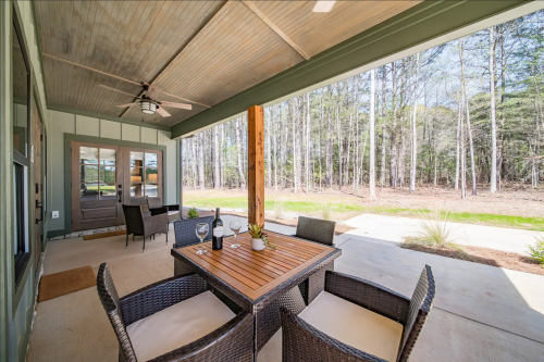 Outdoor patio with a wooden table, four chairs, wine glasses, and a view of trees in the background.