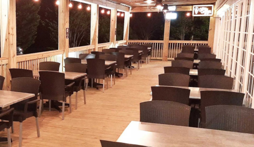 A spacious outdoor dining area with wooden flooring, empty tables, and string lights overhead.