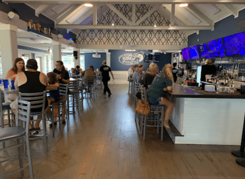 A lively bar scene with patrons seated at the counter and tables, featuring a blue-themed decor and a bartender in motion.