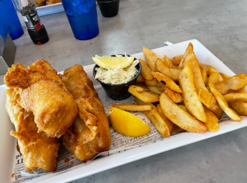 A plate of crispy fried fish with lemon, coleslaw, and golden-brown fries on a white tray.