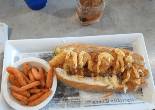 A sandwich filled with fried shrimp and sauce, served with a side of seasoned carrots on a white plate.