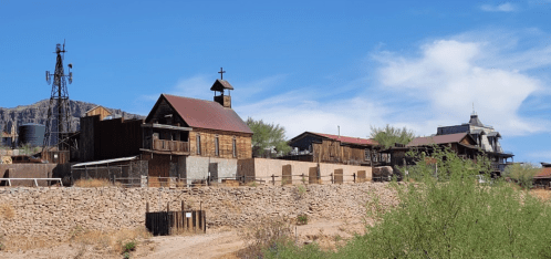 A rustic ghost town with wooden buildings, a church, and a windmill against a clear blue sky and desert landscape.