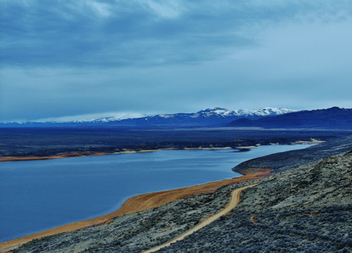 A serene landscape featuring a winding river, mountains in the distance, and a cloudy sky.