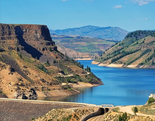 A serene landscape featuring a river winding through rocky hills and mountains under a clear blue sky.