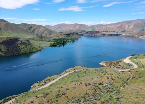 A scenic view of a calm lake surrounded by green hills and mountains under a clear blue sky.