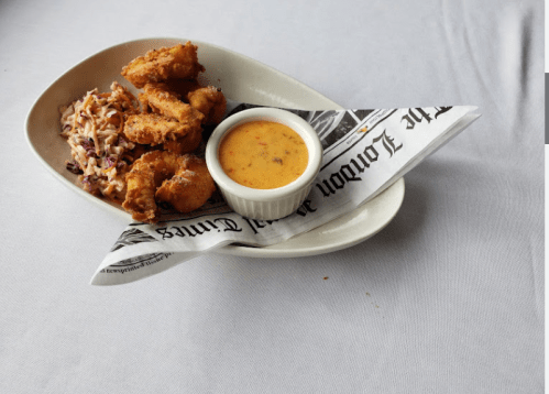 A plate of fried chicken with coleslaw and a small bowl of dipping sauce, served on a newspaper-lined dish.