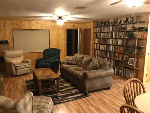 Cozy living room with wooden walls, a bookshelf, comfortable seating, and a coffee table on a patterned rug.