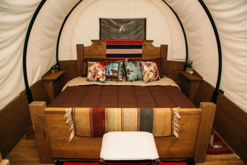 Cozy interior of a glamping tent featuring a wooden bed with decorative pillows and a colorful blanket.