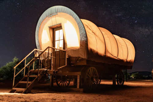 A vintage wagon with a curved roof, illuminated at night under a starry sky.