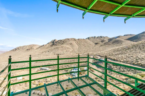 View from a green observation deck overlooking a mountainous desert landscape with sparse vegetation.