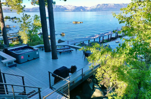 A serene lakeside deck with seating, a hot tub, and stunning mountain views across the water.