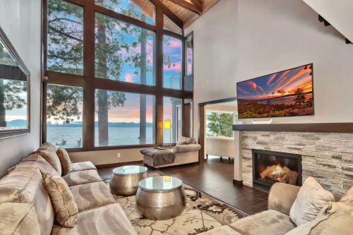 Modern living room with large windows, lake view, cozy seating, and a fireplace, bathed in warm sunset light.