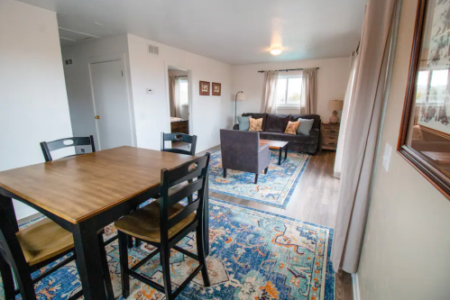 Cozy living space featuring a dining table, sofa, and decorative rug in a well-lit room.