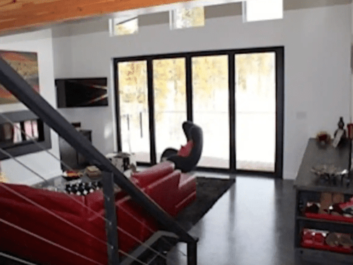 Modern living room with red furniture, large windows, and a view of nature. Sleek design with a cozy atmosphere.