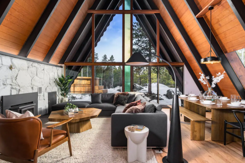 Cozy A-frame living room with large windows, modern furniture, and a snowy outdoor view. Warm and inviting atmosphere.