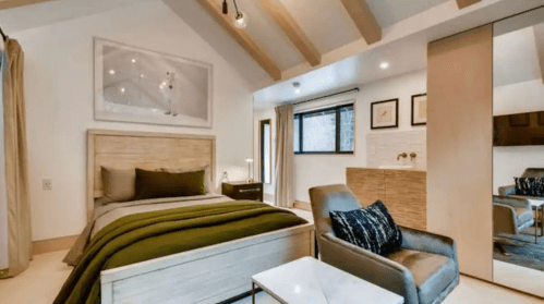 Cozy bedroom with a bed, green bedding, a chair, and large windows, featuring modern decor and wooden beams.