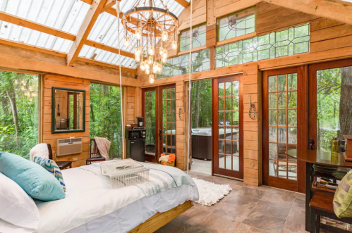 Cozy wooden bedroom with large windows, a chandelier, and a view of greenery outside.