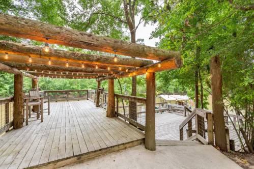 A wooden deck surrounded by trees, featuring string lights and a staircase leading down to a lower area.