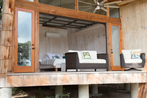 A modern cabin with wooden walls, featuring a cozy seating area and large glass doors opening to the outdoors.