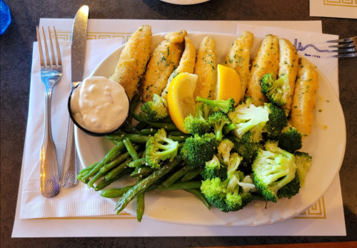 A plate with breaded fish fillets, lemon wedges, and a side of steamed broccoli and green beans, with tartar sauce.