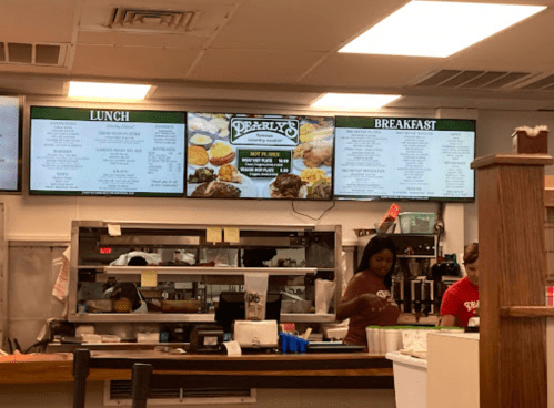 A restaurant counter with staff, displaying lunch and breakfast menus on screens above.