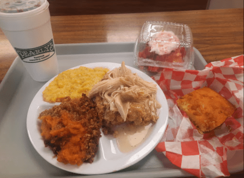 A tray with a plate of chicken, cornbread, sweet potatoes, macaroni, and a dessert, alongside a drink in a cup.
