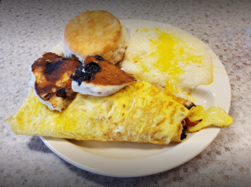 A plate with a fluffy omelette, biscuit, pancakes, and a serving of grits with melted butter.