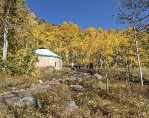 A yurt surrounded by vibrant autumn trees and rocky pathways in a serene outdoor setting.