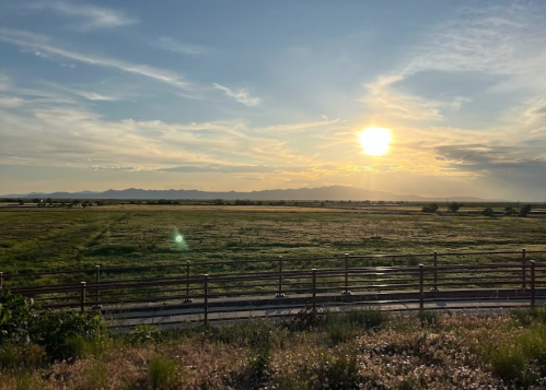 Sunset over a grassy field with distant mountains and a wooden fence in the foreground.