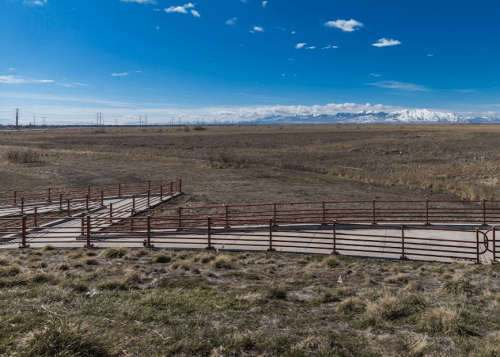 A wide, open landscape with a winding metal path and distant snow-capped mountains under a clear blue sky.