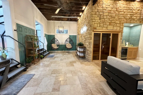 A spacious interior with stone walls, hanging chairs, and green doors, featuring natural light and modern decor.