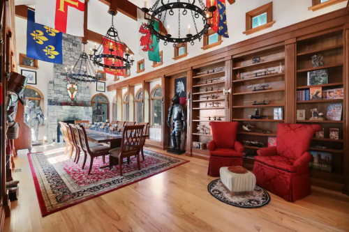 A spacious room with a long dining table, red chairs, banners, and shelves displaying collectibles and a suit of armor.