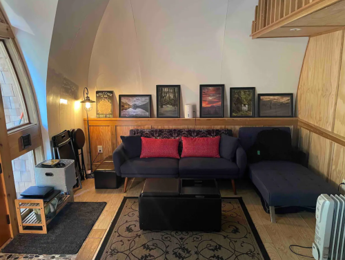 Cozy living area with a blue sofa, red cushions, wooden accents, and framed nature artwork on the walls.