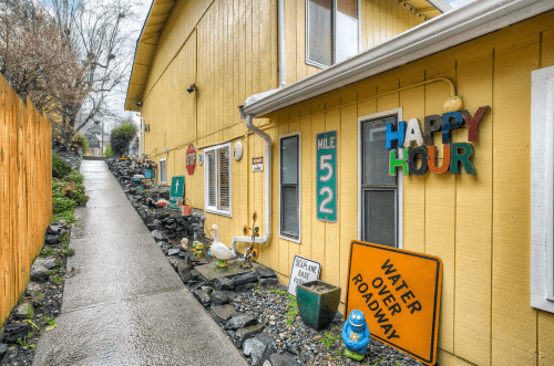 A yellow building with a sloped pathway, colorful signs, and decorative items along the side.