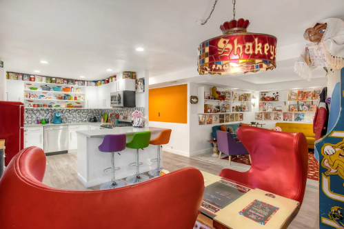 Colorful retro-themed living space with a kitchen, vibrant chairs, and walls adorned with collectibles and artwork.
