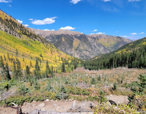 A scenic mountain landscape with vibrant autumn foliage, rolling hills, and a clear blue sky.