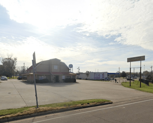 A large, empty parking lot in front of a building with a sign, under a bright sky with scattered clouds.