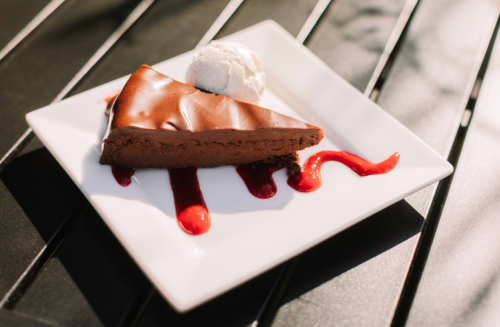 A slice of chocolate cake on a white plate, drizzled with sauce and served with a scoop of ice cream.