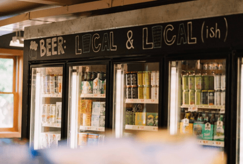 Refrigerated display of various local beers with a sign reading "Beer: Local & Local(ish)."