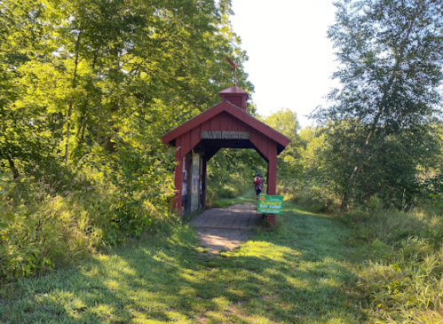 A red wooden welcome archway surrounded by greenery, leading into a nature trail.