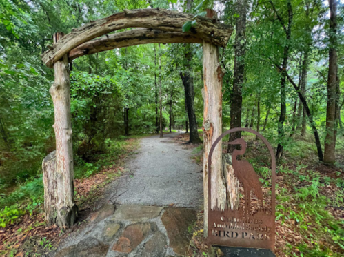 A wooden archway marks the entrance to a nature trail, with a sign indicating "Bird Park" amidst lush greenery.