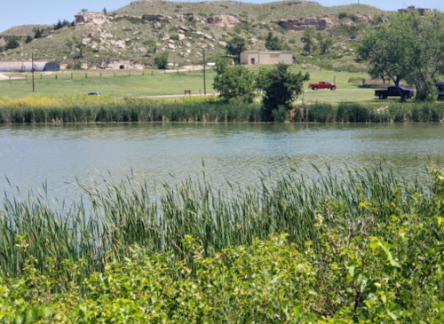 A serene landscape featuring a calm lake, lush greenery, and distant hills under a clear blue sky.