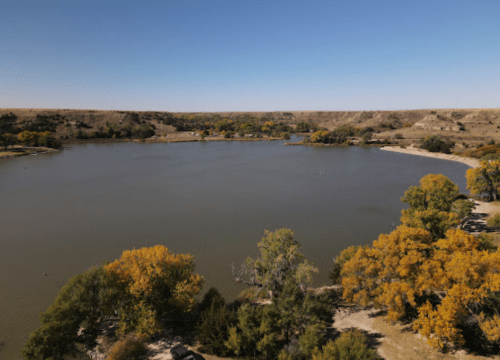 A serene river scene surrounded by autumn trees and rolling hills under a clear blue sky.