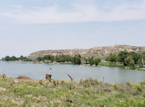 A serene lake surrounded by greenery and hills under a clear blue sky.