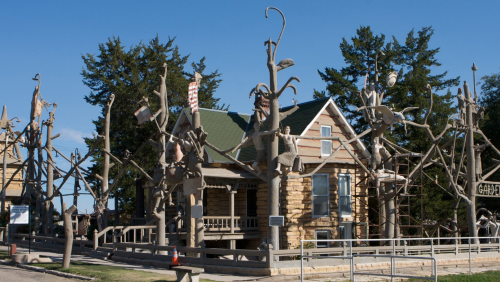 A unique house surrounded by whimsical tree sculptures and art installations against a clear blue sky.
