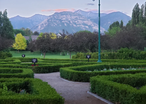 A scenic garden with neatly trimmed hedges and mountains in the background under a colorful sky at dusk.