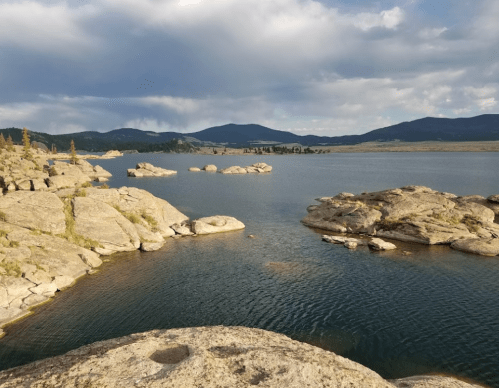 A serene lake surrounded by rocky shores and distant mountains under a partly cloudy sky.