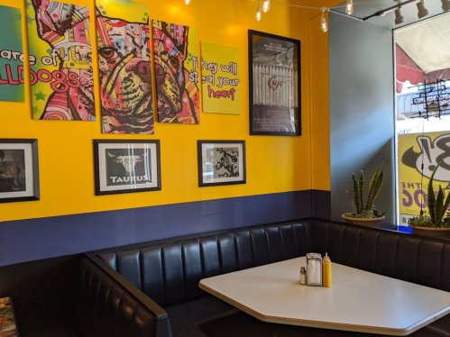 Colorful restaurant interior featuring dog-themed artwork, a black booth, and a bright yellow wall.