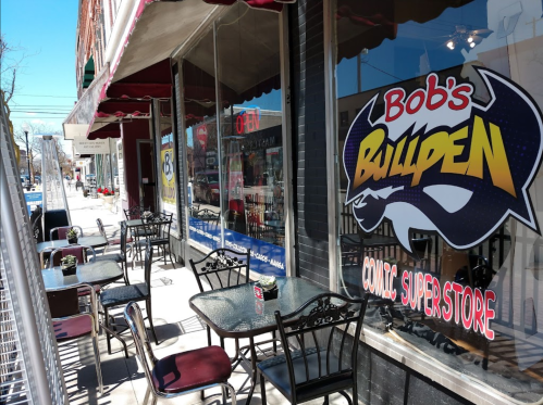 Outdoor seating area in front of Bob's Bullpen Comic Super Store, featuring tables and chairs along a sidewalk.